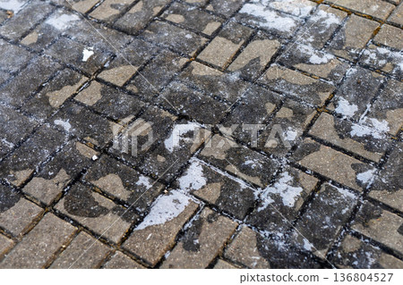 Wet snow and stains on urban pavement. Closeup of melting snow with stains on city sidewalks 136804527