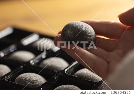 Artisan chocolatier selects textured cocoa truffle for tasting on warm wooden surface 136804535