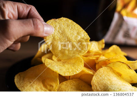 Intimate photograph capturing fingers clutching crispy salted delicacy under warm lighting 136804537