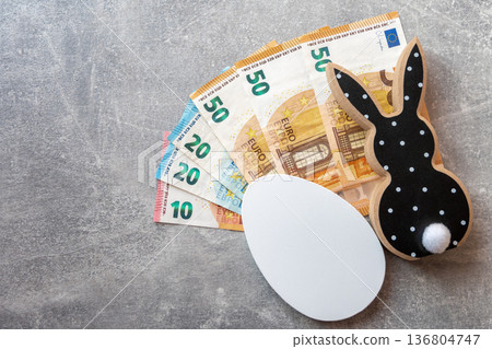 Black and white wood rabbit and egg with cash euro money for easter celebration on the stone background. Shopping of Easter holidays. Space for text. Black and white wood rabbit and egg with cash euro money for easter celebration on the stone background. Shopping of Easter holidays. Space for text. 136804747