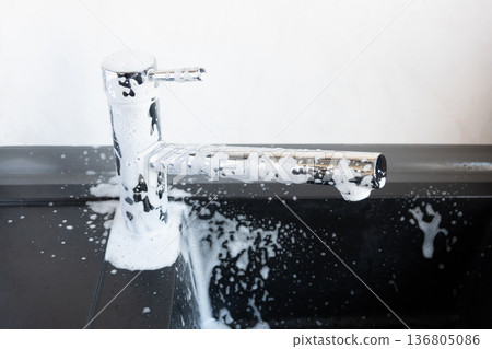 White foam for clean of water dripping of lime on metal tap. Cleaning of the house. Durty faucet in kitchen. White foam for clean of water dripping of lime on metal tap. Cleaning of the house. Durty faucet in kitchen. 136805086
