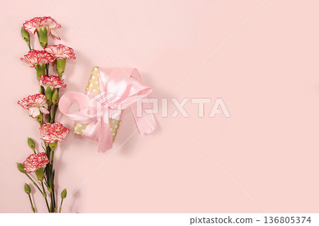 Carnations with a gift on a pink table, abstract spring floral background. Creative modern bouquet, minimal holiday concept. Greeting card for Women's Day or Mother's Day, 136805374