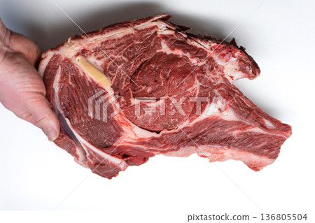 Raw beef ribeye steak held by a hand. Fresh red meat cut with bone and marbling isolated on white background Raw beef ribeye steak held by a hand. Fresh red meat cut with bone and marbling isolated on white background 136805504