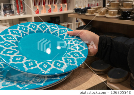 Person selecting blue patterned plate in store 136805548