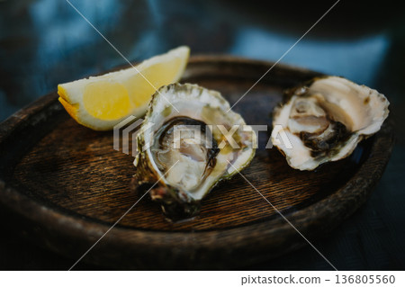 Two fresh oysters with lemon slice on a wooden plate in a fish restaurant. Two fresh oysters with lemon slice on a wooden plate in a fish restaurant. 136805560