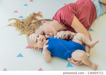 Mother and baby lying on a soft play mat at home, playing, talking and sharing a joyful moment together. Authentic family lifestyle, early childhood development and emotional bonding. Parenting and 136805711