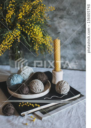 Balls of wool yarn, needles for hand knitting and bouquet of Mimosa flowers on a table. 136805748