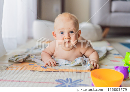 Little baby playing with toys on a soft baby play mat at home. Early childhood development, sensory play, learning through play, curiosity, and happy infant activity concept for modern parenting. 136805779