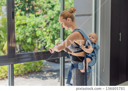 Mother doing fitness exercises while holding her baby at home, combining workout and childcare. Real lifestyle moment showing balance, strength and love. Postpartum fitness, healthy motherhood and Mother doing fitness exercises while holding her baby at home, combining workout and childcare. Real lifestyle moment showing balance, strength and love. Postpartum fitness, healthy motherhood and 136805781