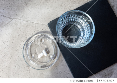 Pill and glass with water on the stone table. Healthcare from pharmacy. Person sit at home because of illness. 136805807