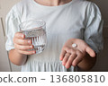 Pill and glass with water in the hand of child. Healthcare from pharmacy. Kid sit at home because of illness. 136805810