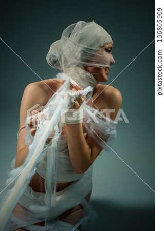 Woman wrapped in bandages expressing anguish, struggling to break free. Conceptual art of confinement and suffering. 136805909