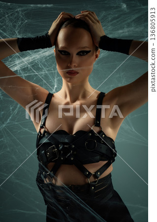 Powerful woman in black harness with dramatic makeup posing in spiderwebs 136805913