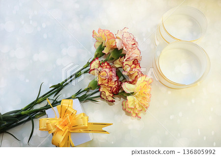 A bouquet of flowers with a festive ribbon and a gift on a light background, congratulations on the holiday 136805992