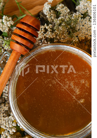 fresh natual flower honey in glass jar with wooden  honey spoon around herb flowers. macro 136806101