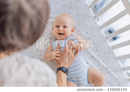 Father gently placing his baby into a crib at home, creating a calm and safe bedtime moment. Caring fatherhood scene filled with trust and warmth. Parenting, infant sleep and family bonding concept Father gently placing his baby into a crib at home, creating a calm and safe bedtime moment. Caring fatherhood scene filled with trust and warmth. Parenting, infant sleep and family bonding concept 136806139
