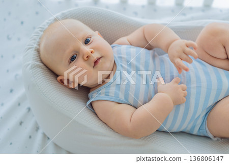 Baby lying peacefully in a cozy cocoon nest inside a crib, feeling safe and calm at home. Soft light and warm atmosphere highlight comfort and care. Infant sleep, safety and gentle parenting concept Baby lying peacefully in a cozy cocoon nest inside a crib, feeling safe and calm at home. Soft light and warm atmosphere highlight comfort and care. Infant sleep, safety and gentle parenting concept 136806147