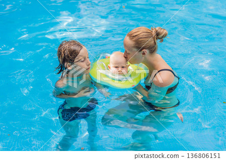 Mother with her older son and baby wearing a neck float enjoying time together in a swimming pool. Happy family water activity full of care and fun. Summer parenting, baby swimming and family bonding Mother with her older son and baby wearing a neck float enjoying time together in a swimming pool. Happy family water activity full of care and fun. Summer parenting, baby swimming and family bonding 136806151
