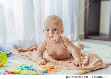 Little baby playing with toys on a soft baby play mat at home. Early childhood development, sensory play, learning through play, curiosity, and happy infant activity concept for modern parenting. Little baby playing with toys on a soft baby play mat at home. Early childhood development, sensory play, learning through play, curiosity, and happy infant activity concept for modern parenting. 136806152