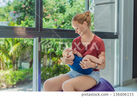 Young mother gently rocks her baby on a fitness ball at home, creating a calm loving atmosphere. Authentic family lifestyle, natural parenting and emotional bonding. Motherhood, wellbeing and baby Young mother gently rocks her baby on a fitness ball at home, creating a calm loving atmosphere. Authentic family lifestyle, natural parenting and emotional bonding. Motherhood, wellbeing and baby 136806155
