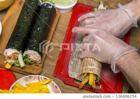 Process of making sushi and rolls. Close-up of man chef hands preparing traditional Japanese food at home or in restaurant on kitchen table. Process of making sushi and rolls. Close-up of man chef hands preparing traditional Japanese food at home or in restaurant on kitchen table. 136806254