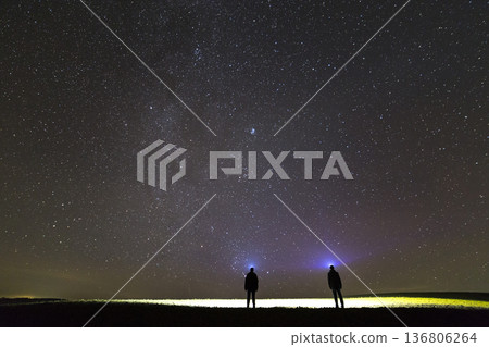 Back view of two men with head flashlights on green grassy field under dark blue summer starry sky. 136806264