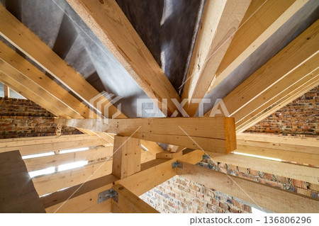 Attic of a building under construction with wooden beams of a roof structure and brick walls. 136806296