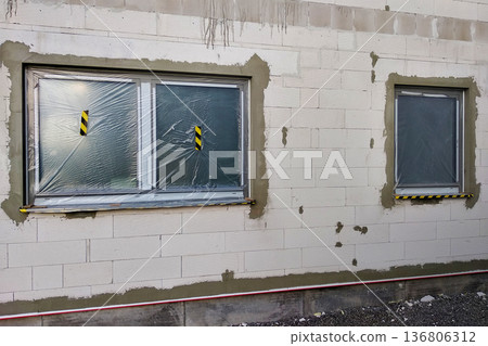Windows of a house under construction covered with protective plastic film. 136806312
