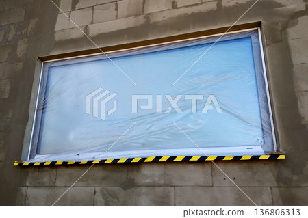 Window of a house under construction covered with protective plastic film. Window of a house under construction covered with protective plastic film. 136806313