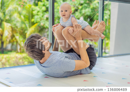 Father exercising with his small baby at home, active parenting and healthy lifestyle. Strong family bond, early physical development, modern fatherhood, fitness with children concept. Father exercising with his small baby at home, active parenting and healthy lifestyle. Strong family bond, early physical development, modern fatherhood, fitness with children concept. 136806489