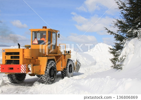 Yellow snowplow clearing a winter road after heavy snowfall. Yellow snowplow clearing a winter road after heavy snowfall. 136806869