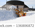 Front loader clears large piles of snow near rural buildings in winter, 136806872