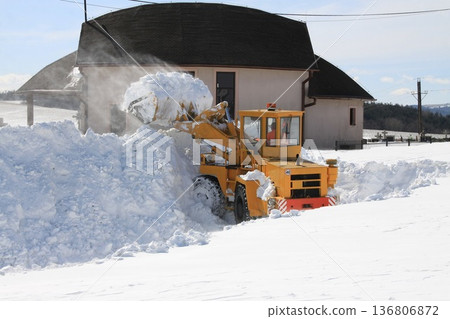 Front loader clears large piles of snow near rural buildings in winter, 136806872