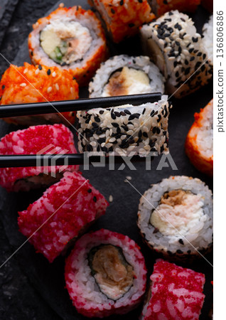 sushi roll in chopsticks beautiful served at black dish. top view. macro shot sushi roll in chopsticks beautiful served at black dish. top view. macro shot 136806886