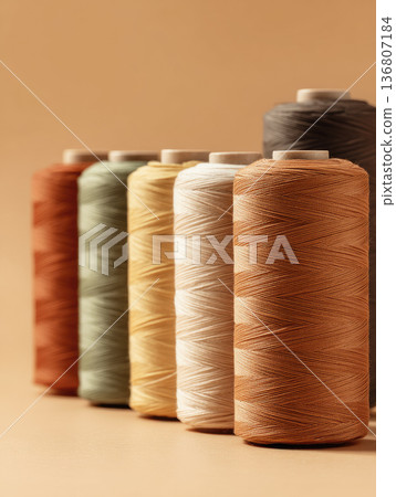 Sustainable textile factory spools of thread in various earthy colors arranged in row on neutral background create calm and organized atmosphere for eco friendly production 136807184