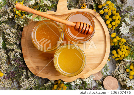 fresh natual different  honey in glass jars with wooden  honey spoon around herb flowers. flat lay 136807476