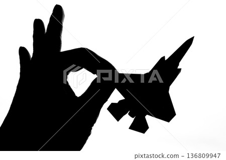 Silhouette of a jet fighter held between fingers 136809947