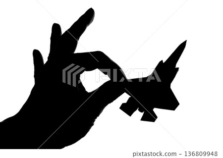 Silhouette of a jet fighter held between fingers 136809948