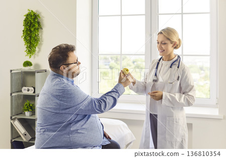 Nutritionist gives apple to patient while discussing healthy diet in clinic 136810354