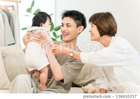 A father holding a baby and a grandmother comforting him in the living room at home A father holding a baby and a grandmother comforting him in the living room at home 136810357