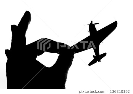 Silhouette of a propeller fighter plane pinched between fingers Silhouette of a propeller fighter plane pinched between fingers 136810392