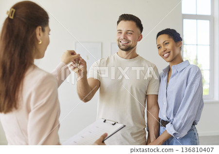 Real estate agent giving keys from new home apartment to happy couple, clients buy or rent property Real estate agent giving keys from new home apartment to happy couple, clients buy or rent property 136810407