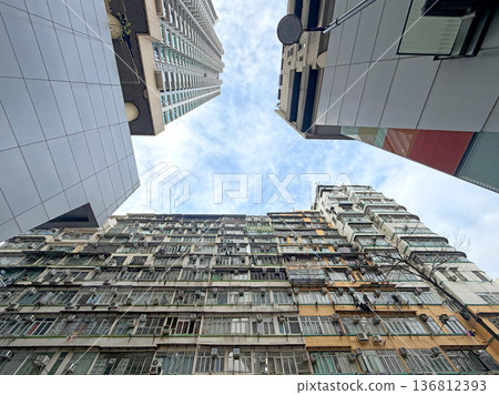 Looking up at contrasting modern and old apartment buildings against a cloudy sky Looking up at contrasting modern and old apartment buildings against a cloudy sky 136812393