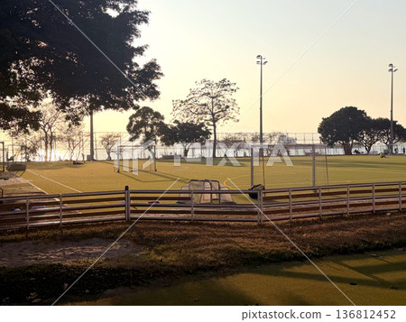 Coastal soccer field at sunset with calm water and distant ship, illuminated by stadium lights Coastal soccer field at sunset with calm water and distant ship, illuminated by stadium lights 136812452