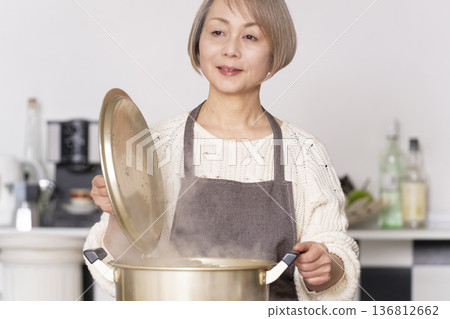 一位老婦人在廚房裡熬豬肉湯，並用碗盛出來。 136812662