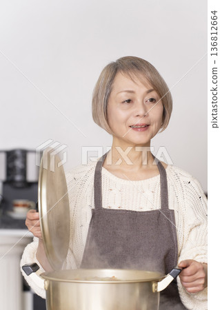 一位老婦人在廚房裡熬豬肉湯，並用碗盛出來。 136812664