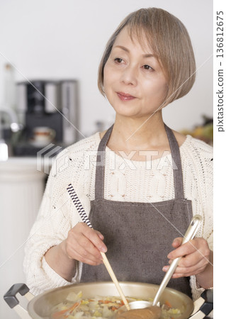 A senior woman making pork soup in the kitchen and serving it in a bowl 136812675
