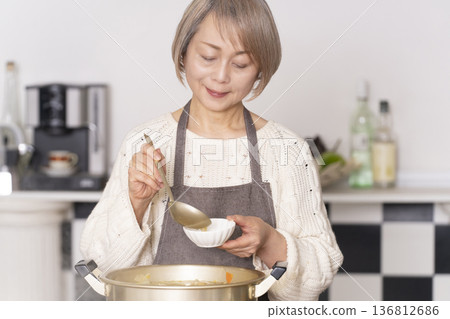 A senior woman making pork soup in the kitchen and serving it in a bowl 136812686