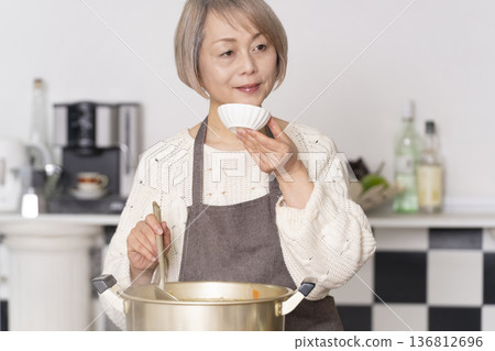 一位老婦人在廚房裡熬豬肉湯,並用碗盛出來。 一位老婦人在廚房裡熬豬肉湯,並用碗盛出來。 136812696
