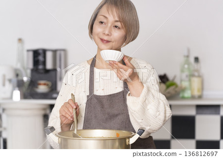 一位老婦人在廚房裡熬豬肉湯，並用碗盛出來。 136812697